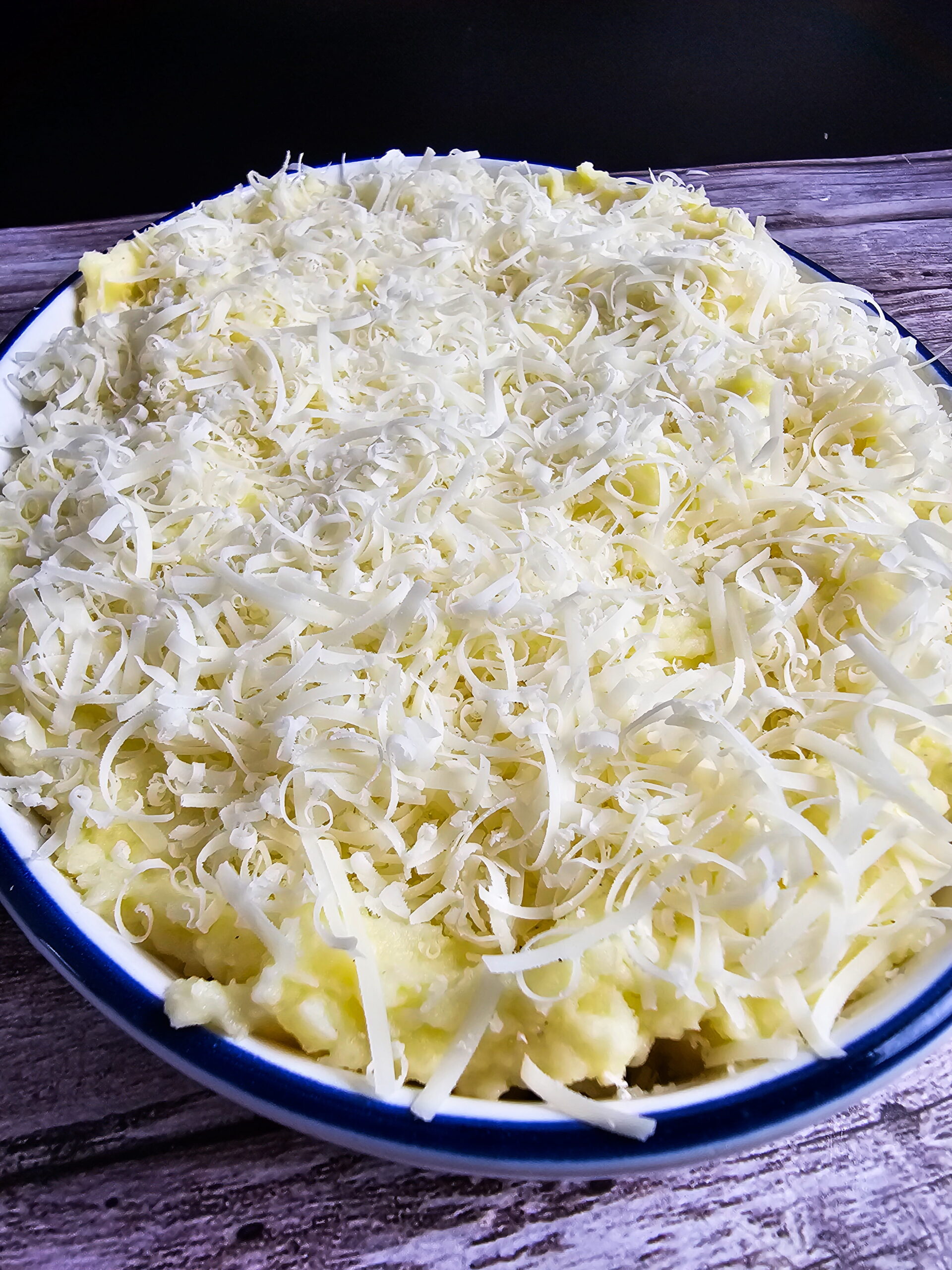 Whipped mashed potatoes transferred to a buttered casserole dish topped with shredded Asiago cheese