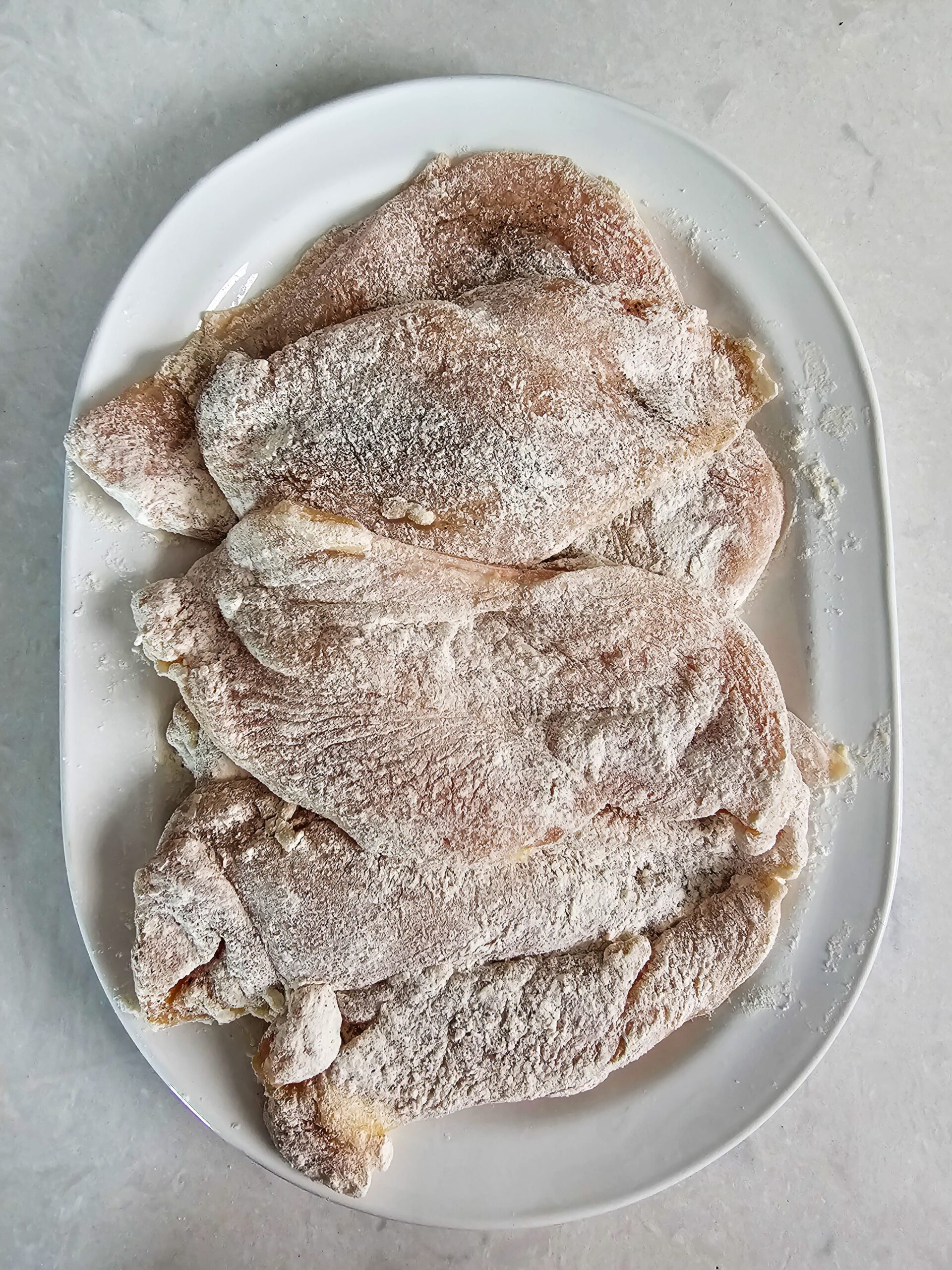Chicken cutlet being dredged in seasoned flour mixture before searing for Marry Me Chicken