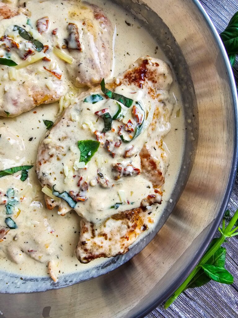 UP CLOSE PHOTO CHICKEN BREASTS IN CREAMY SAUCE GANISHED WITH SUN DRIED TOMATOES AND FRESH BASIL