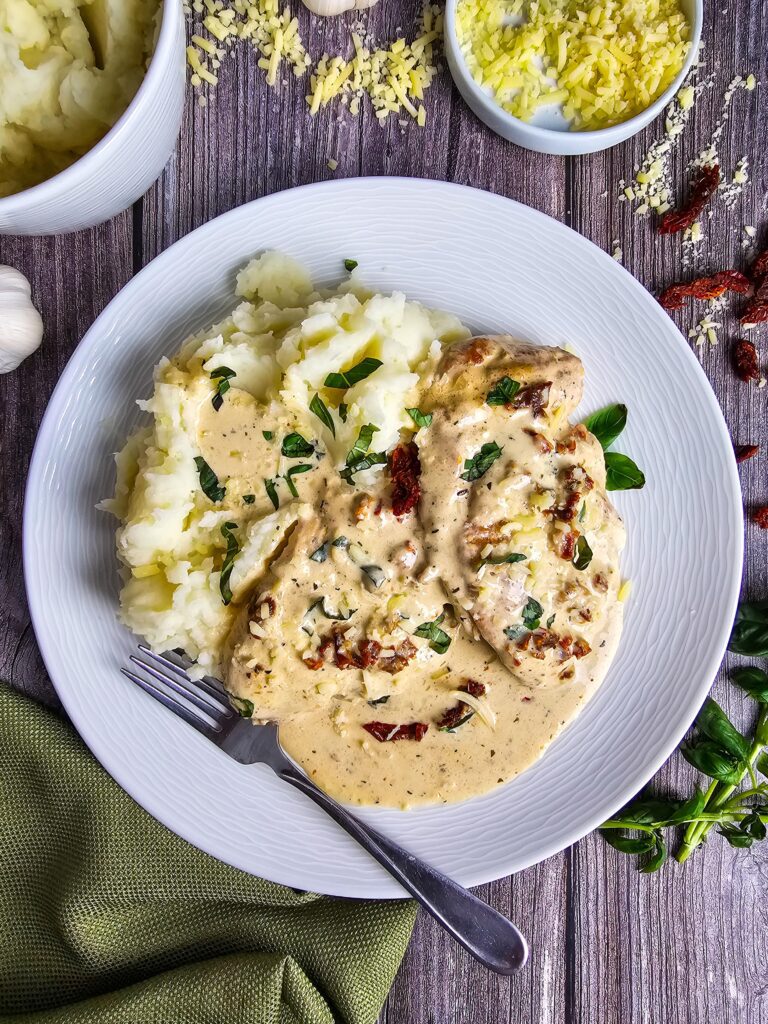 CHICKEN BREASTS PLATED ON A BED OF GARLIC MASHED POTATOES GARNISHED WITH FRESH BASIL AND SUN DRIED TOMATOES