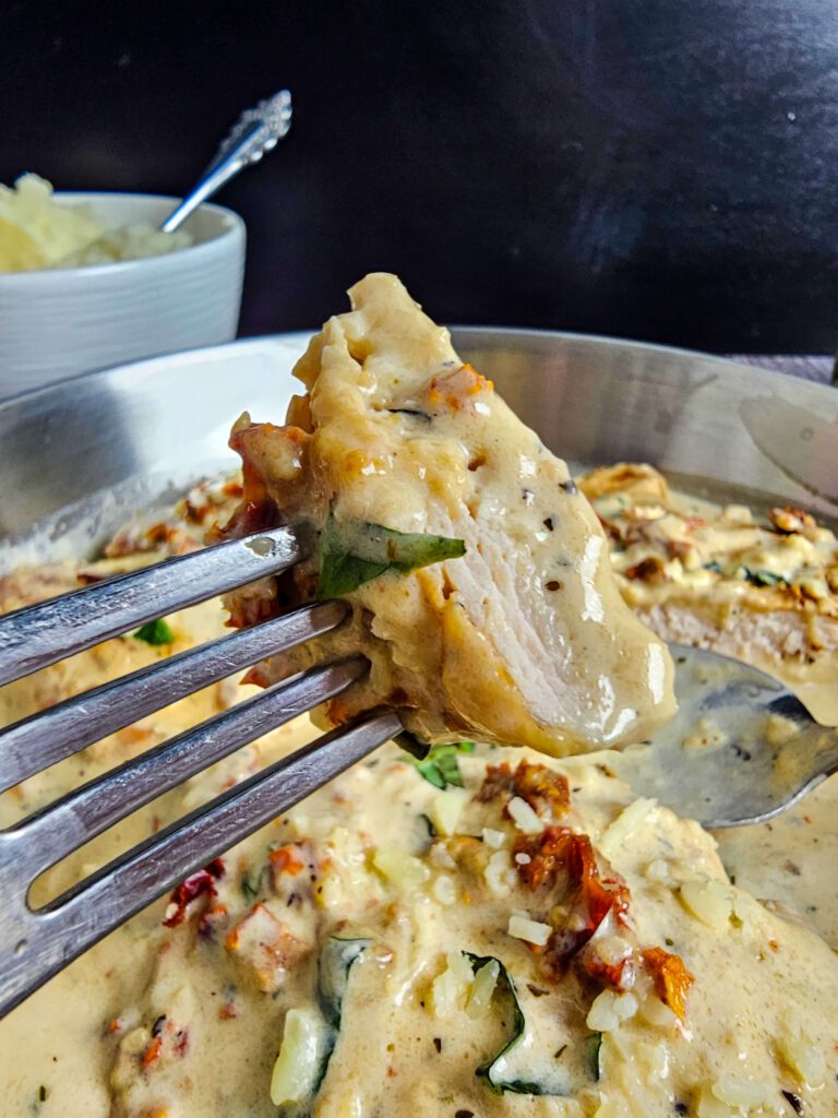 BITE SIZE PIECE OF CHICKEN BREAST ON A FORK DRIPPING WITH CREAMY SAUCE
