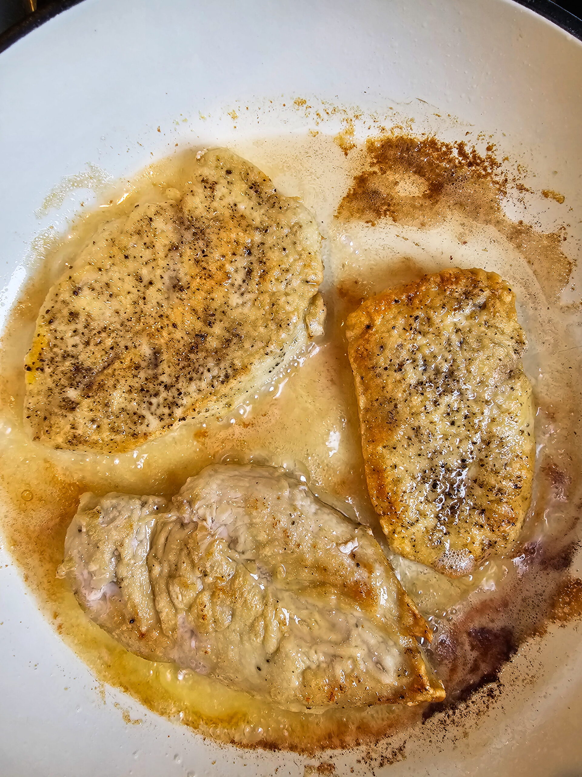 Chicken cutlets searing in butter and olive oil in a hot skillet until golden brown