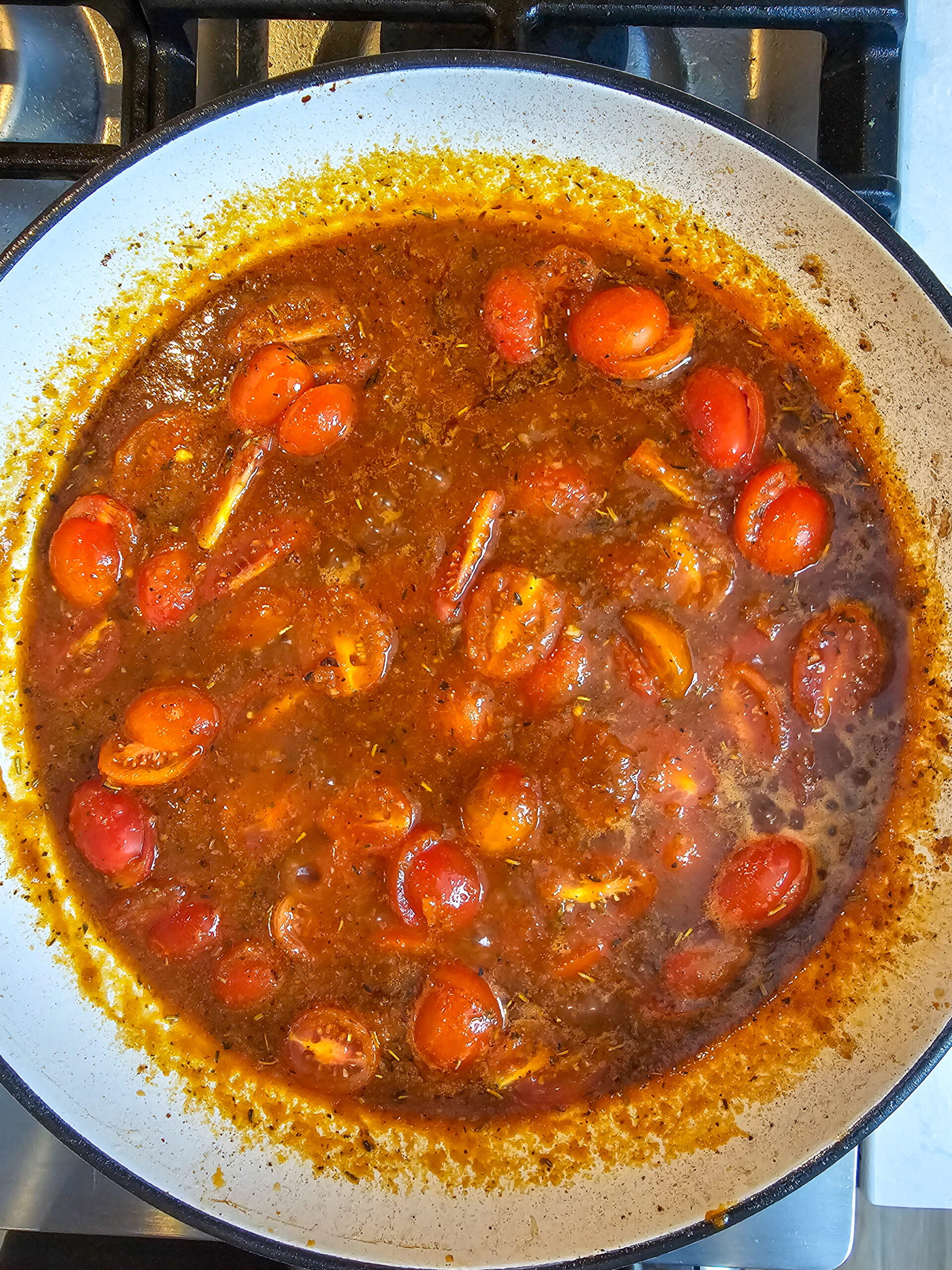 Halved cherry tomatoes added to Italian tomato sauce simmering in a skillet with herbs and broth