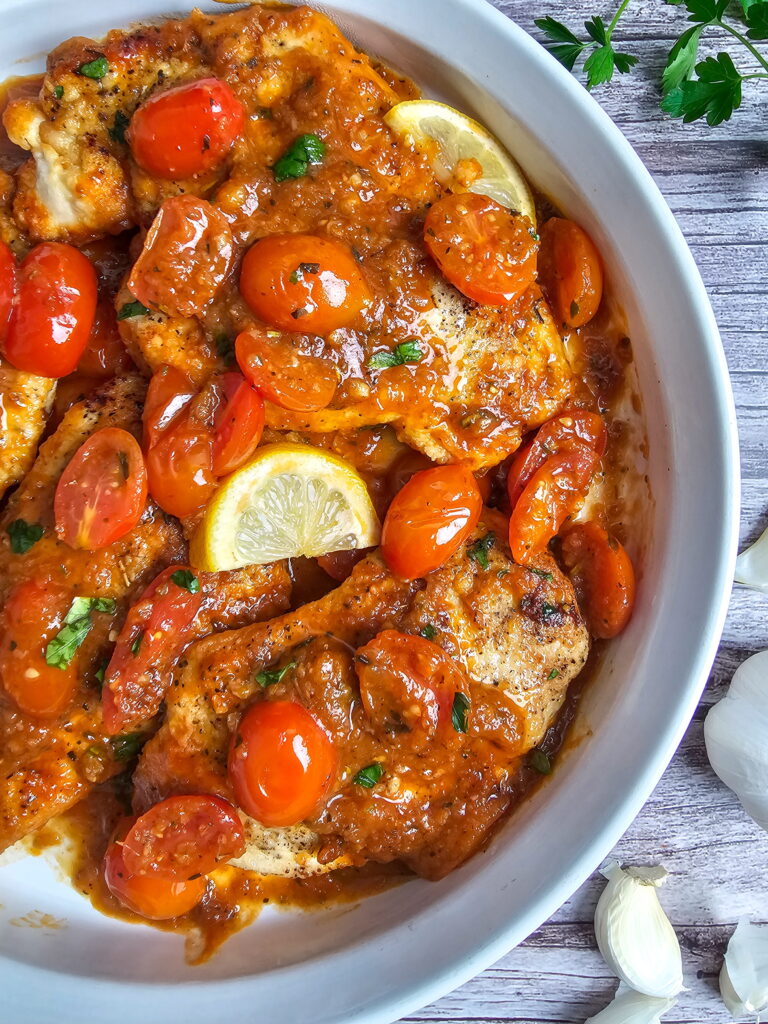 Close-up of silky cherry tomato sauce with chicken cutlets in a white serving dish