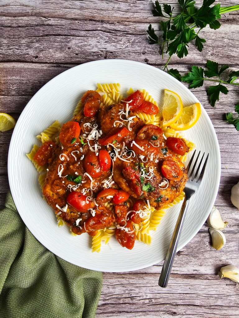 Plated Italian chicken cutlets in cherry tomato sauce with fresh basil and parmesan on top