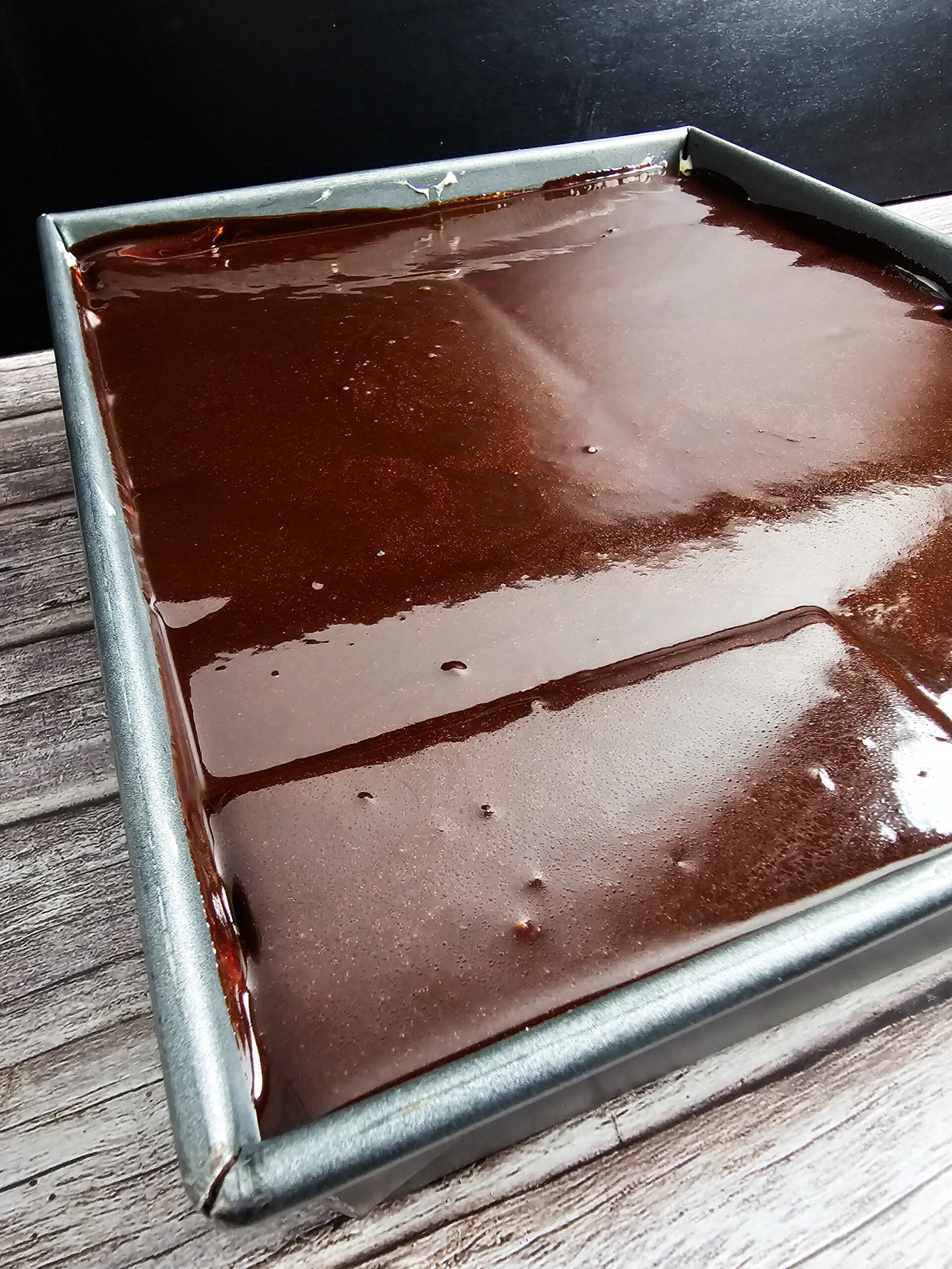 Chocolate fudge topping being poured over top graham cracker layer of eclair cake in lasagna pan