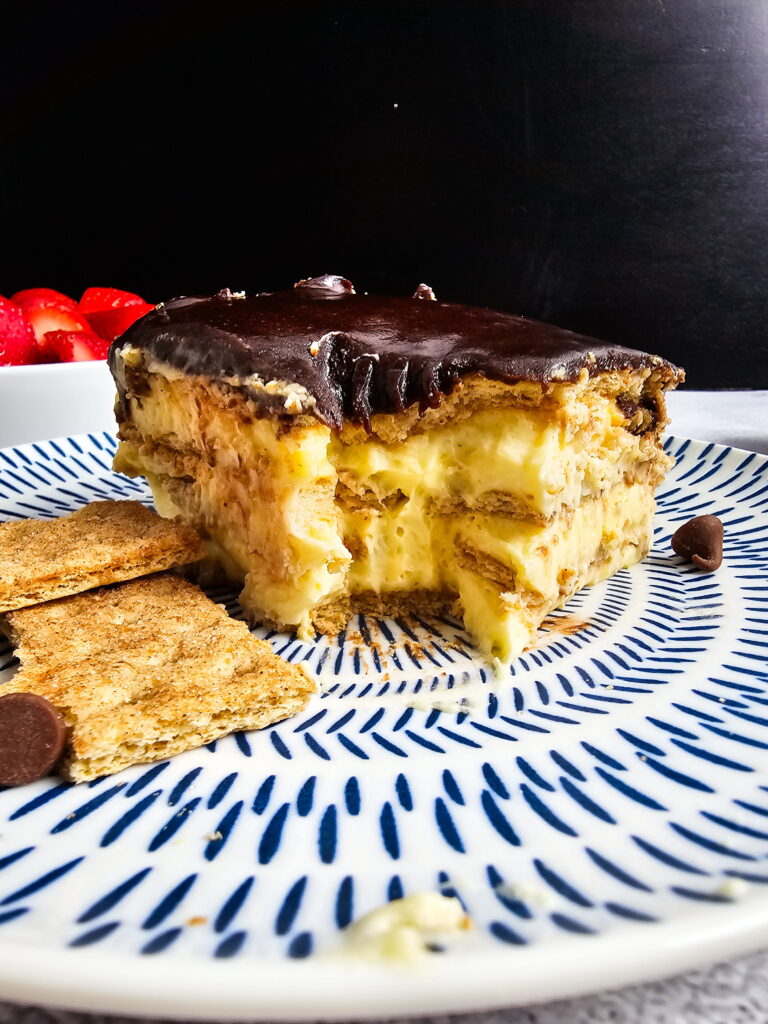 Slice of triple-layer no-bake chocolate eclair cake showing graham cracker layers and vanilla pudding cream filling
