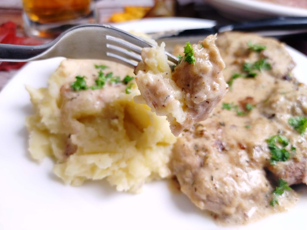CREAMY SMOTHERED PORK CHOPS ON A FORK CLOSE UP PICTURE