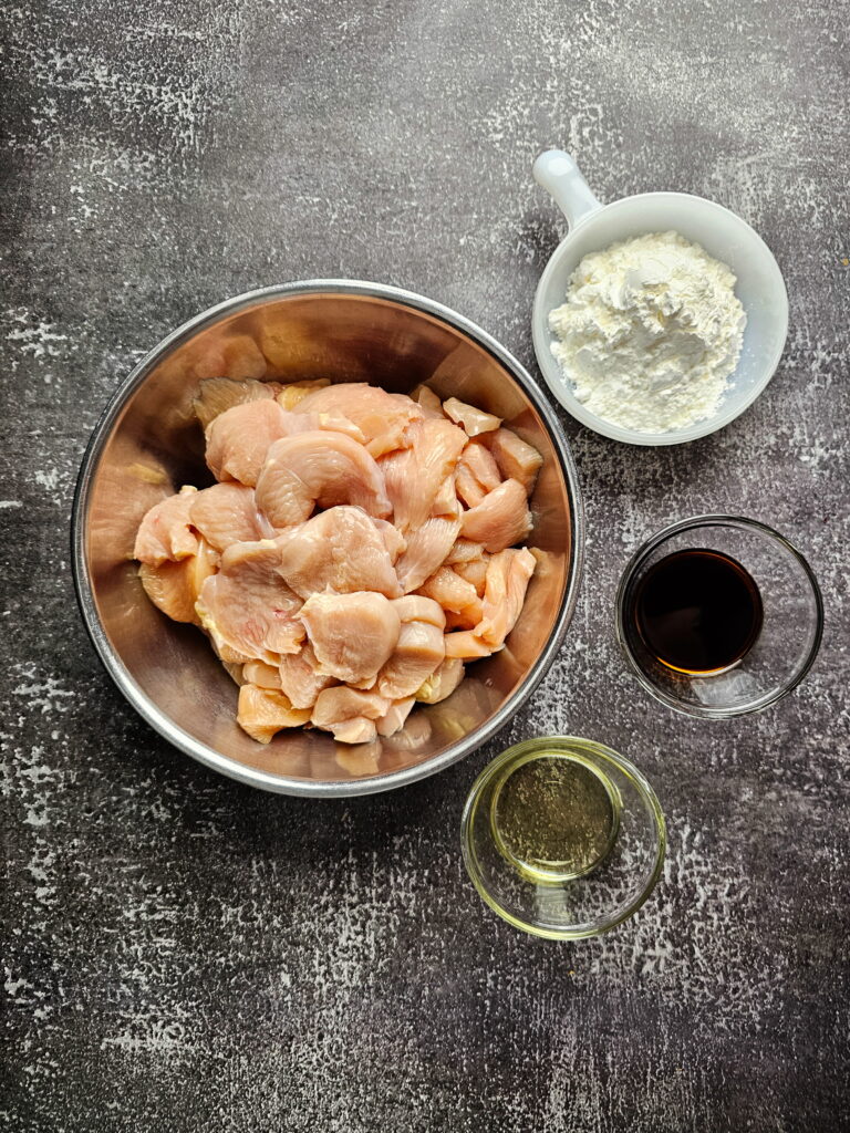 Raw ingredients for Mongolian chicken including sliced chicken breast soy sauce brown sugar garlic ginger and green onions.