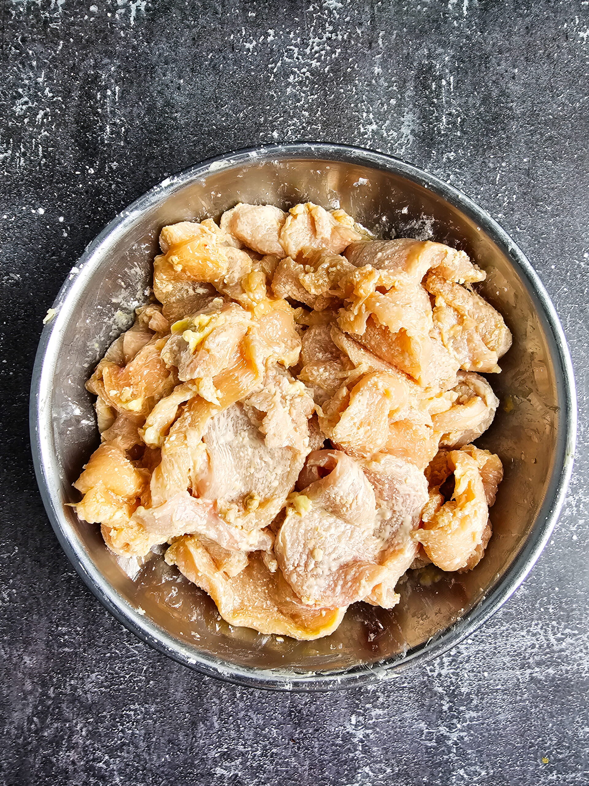 Chicken strips coated in cornstarch marinade during velveting step for tender Mongolian chicken recipe.