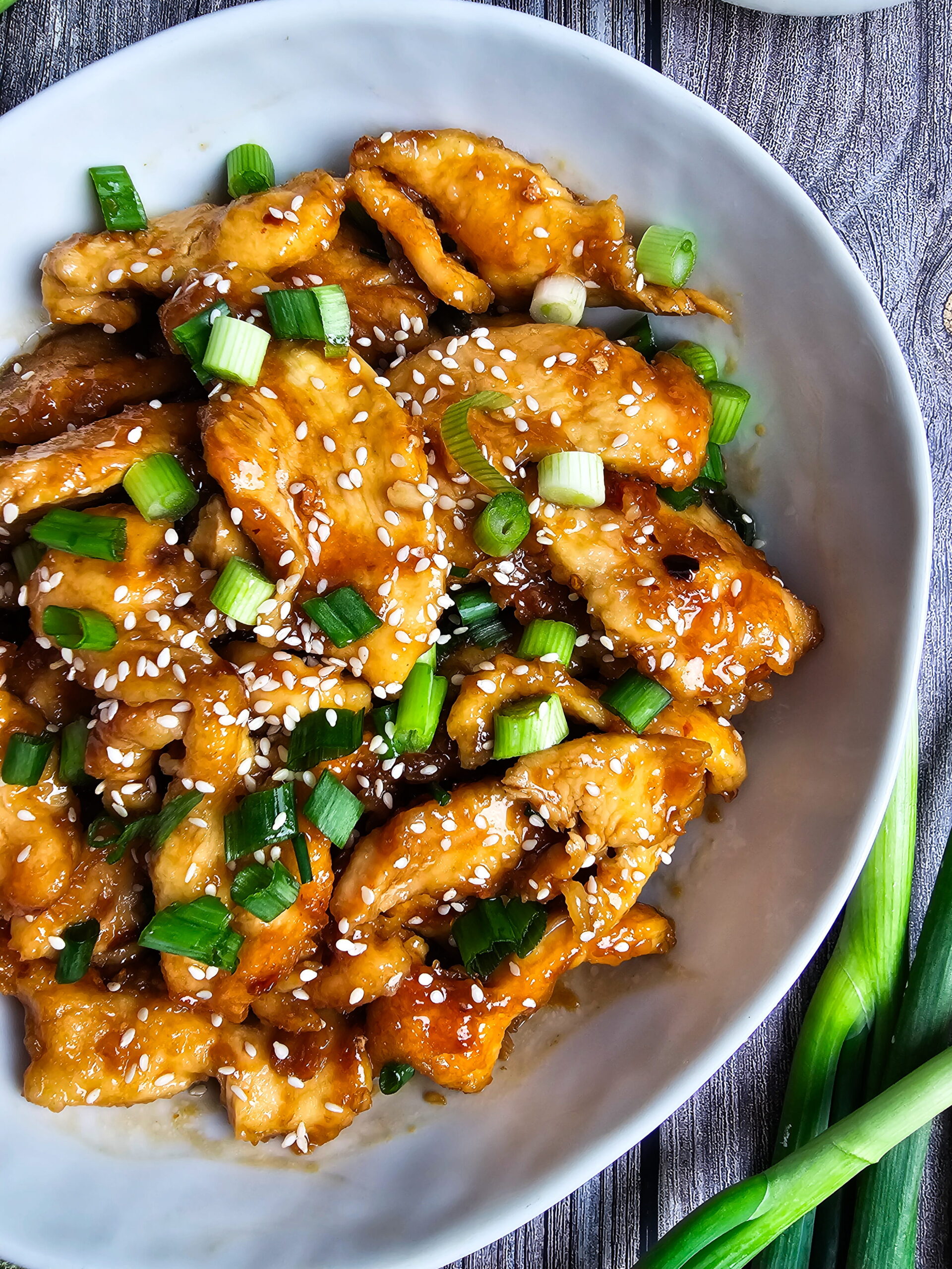 Crispy homemade Mongolian chicken in glossy savory sweet sauce garnished with green onions served in skillet close up.