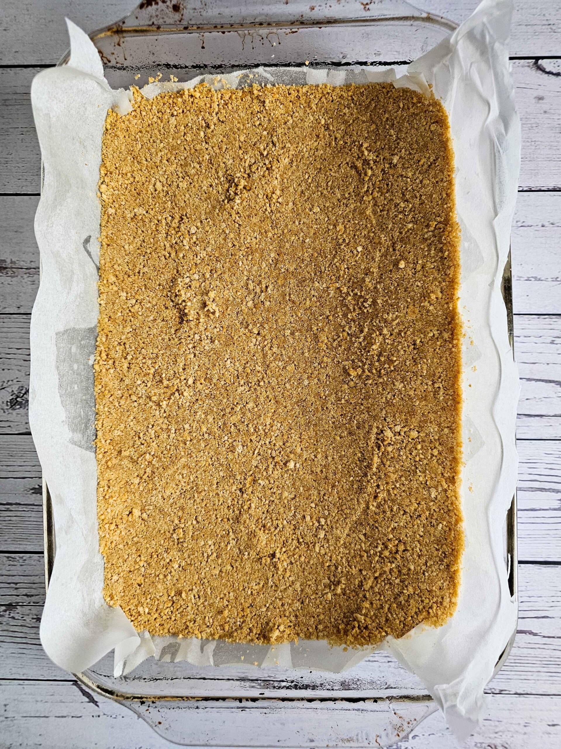 PRESS THE GRAHAM CRACKER CRUST INTO A 9 X 13 BAKING DISH LINED WITH PARCHMENT PAPER