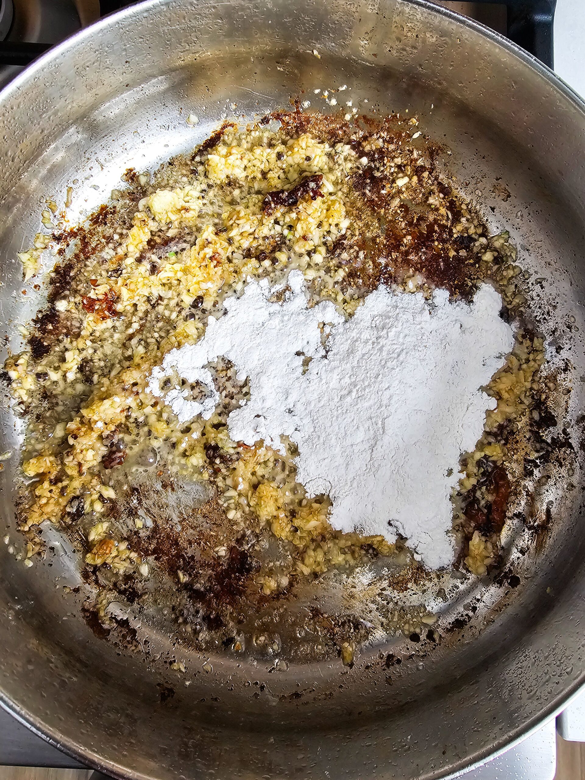 PREPARE THE ROUX AND ADD THE FLOUR TO THE TOASTY GARLIC AND STIR FOR ONE MINUTE