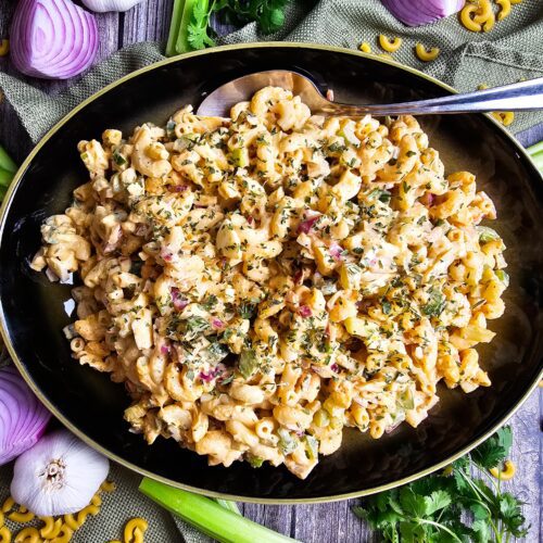 Overhead shot of a summer pasta salad with fresh veggies and herbs in a green serving bowl.