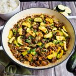 Healthy beef stir fry cooking in a white enamel pan, plated with rice and chopsticks.
