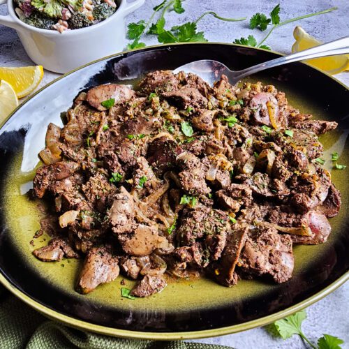 Large green and black platter filled with creamy chicken livers in white wine sauce, garnished with herbs.