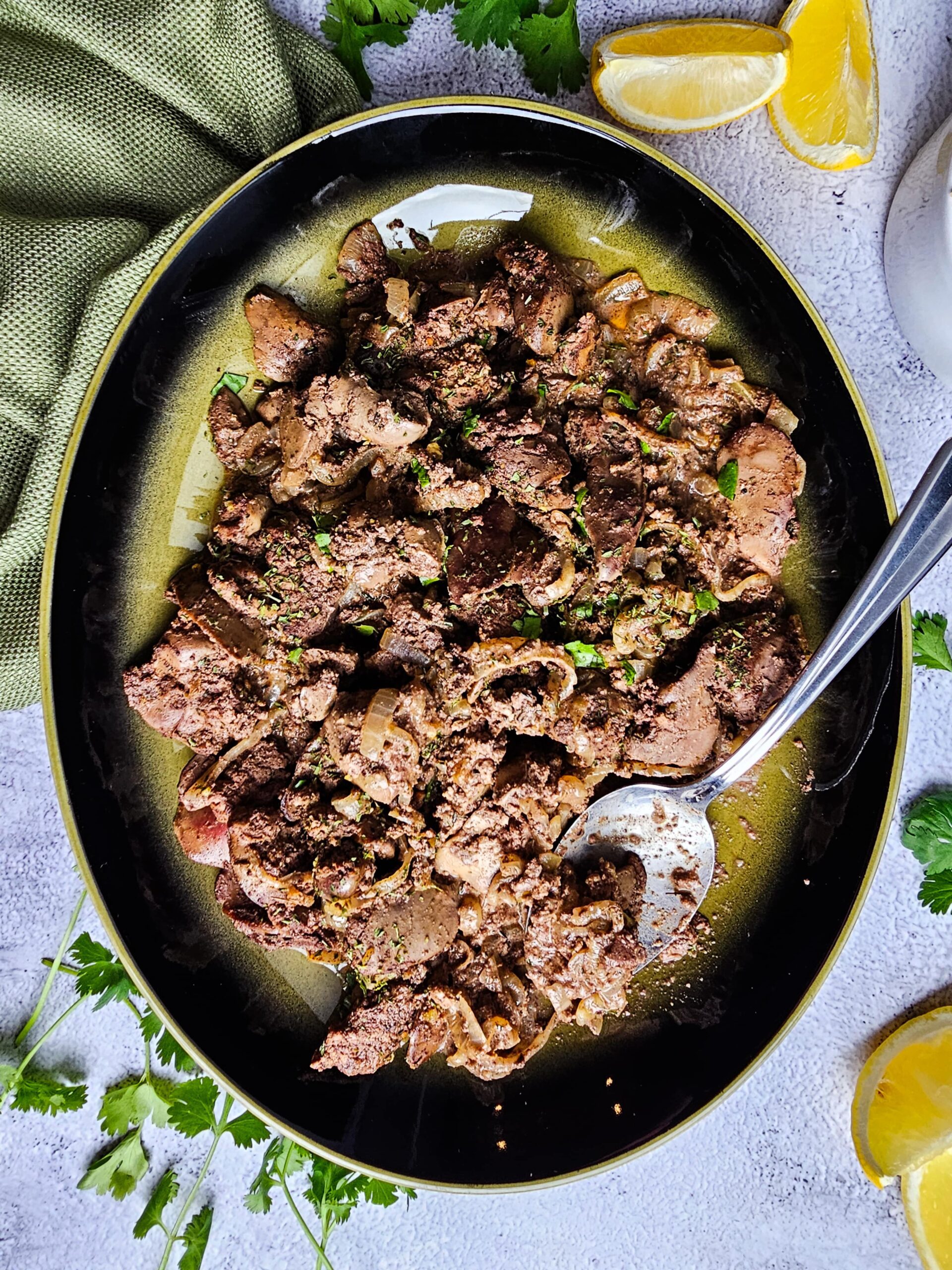 Skillet-style chicken livers plated on a green and black serving dish, topped with fresh herbs.