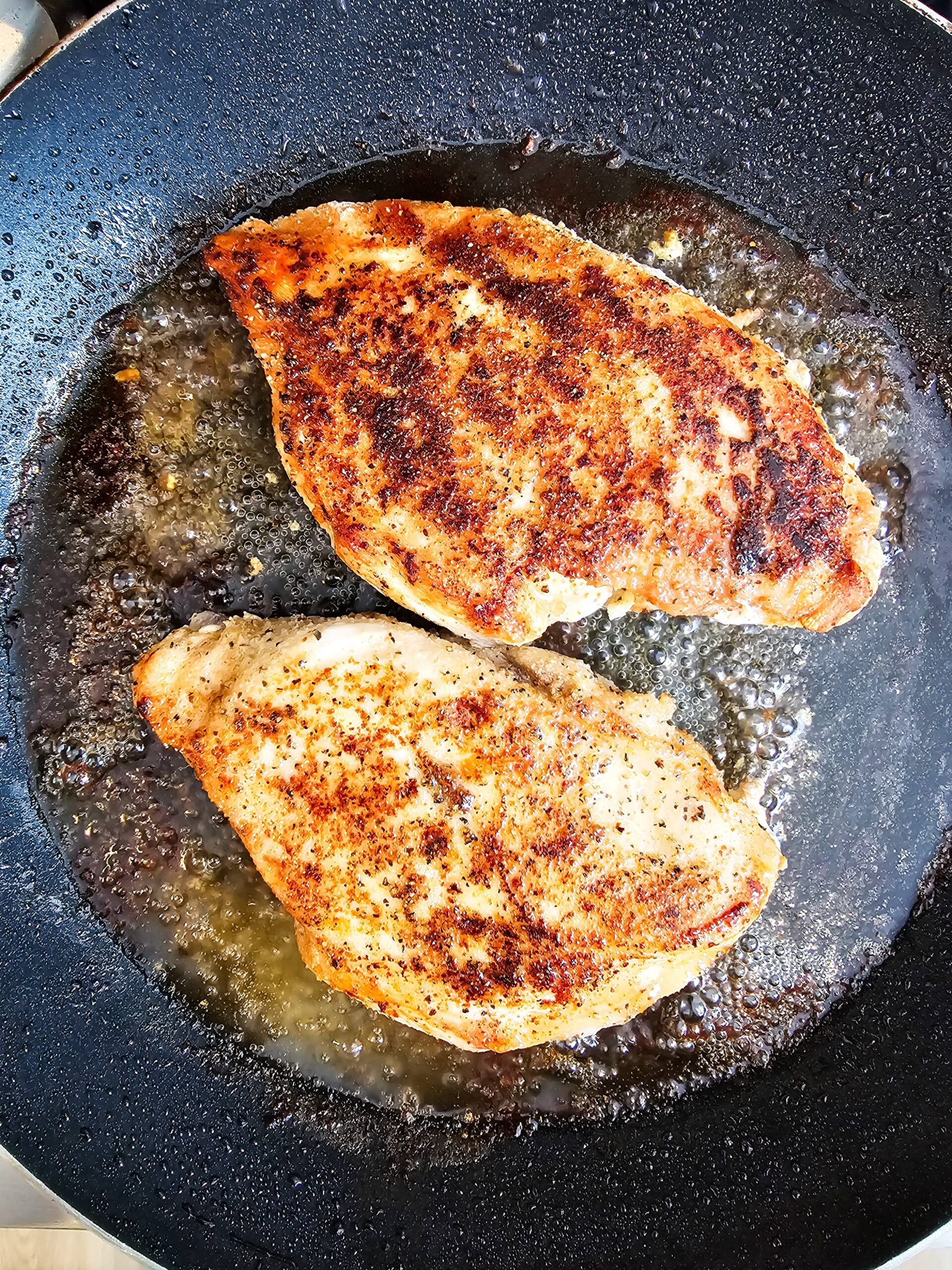 TWO SEASONED CHICKEN BREASTS COOKING IN A SKILLET