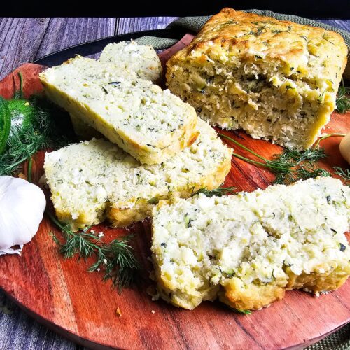 SLICED ZUCCHINI DILL FETA BREAD ON A WOODEN CUTTING BOARD