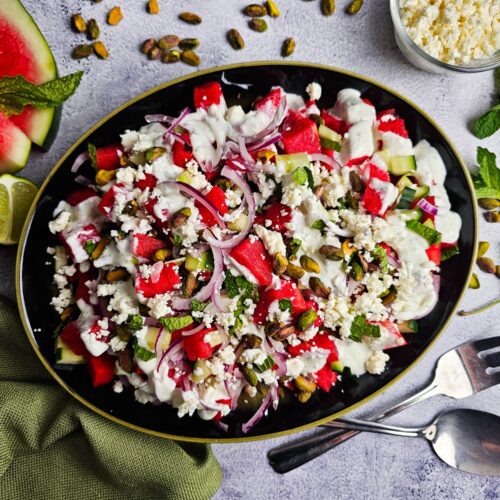 large platter with watermelon salad garnished with watermelon slices and fresh mint