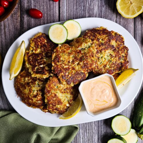 OVAL WHITE SERVING PLATTER LOADED WITH ZUCCHINI FRITTERS AND SMOKED PAPRIKA YOGURT SAUCE