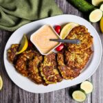 large white serving platter arranged with zucchini fritters and yogurt sauce