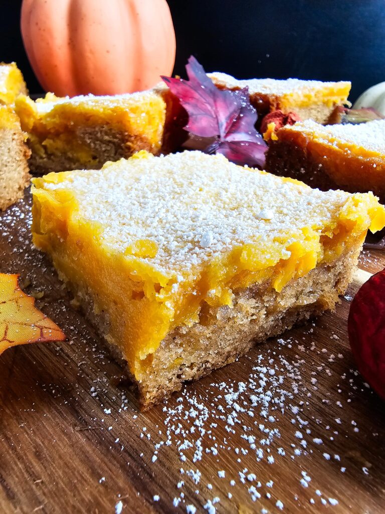 UPCLOSE PUMPKIN BUTTER BAR SPRINKLED WITH POWERED SUGAR ON A WOODEN CUTTING BOARD