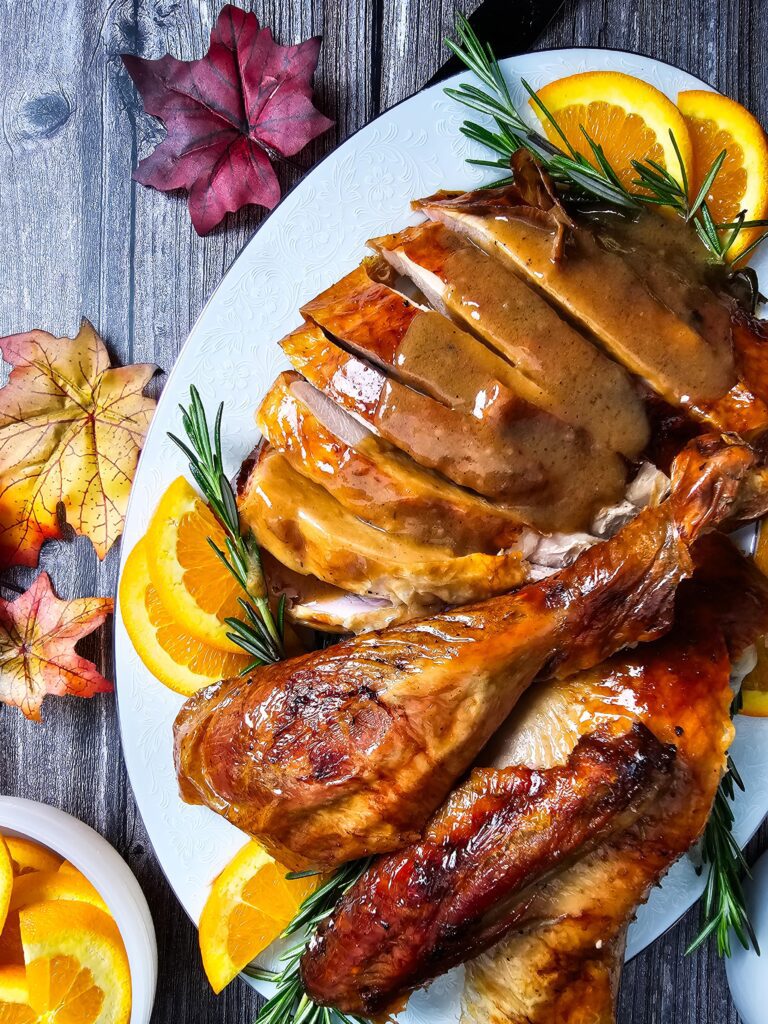 LARGE PLATTER WITH SLICED TURKEY BREAST DRIZZLED IN GRAVY AND A LARGE LEG AND OTHER CARVED TURKEY PARTS