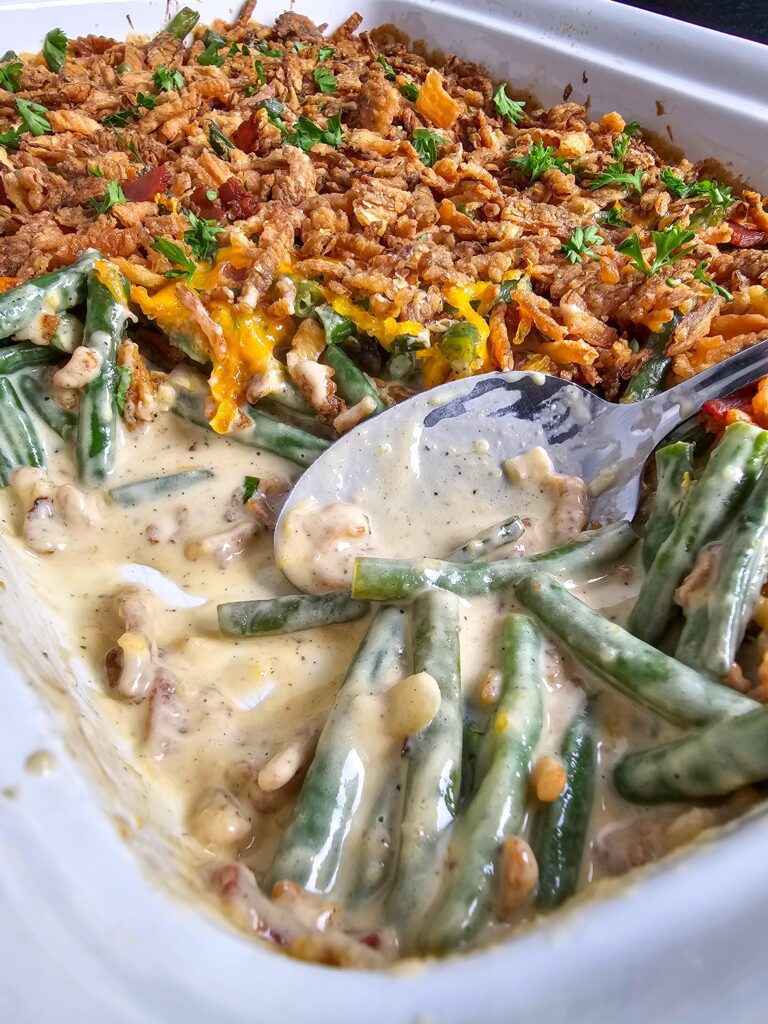 SIDE VIEW OF THE ENTIRE BAKING DISH WITH A SCOOPE OF GREEN BEAN CASSEROLE.