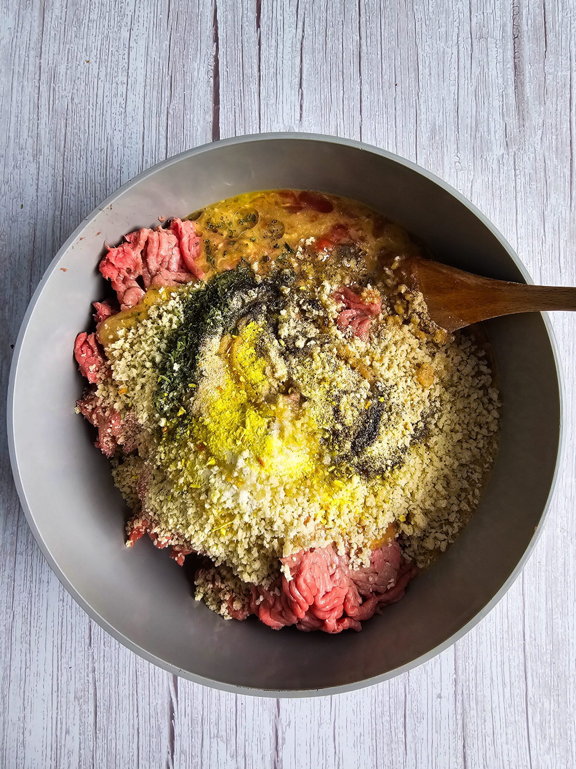 Gently mixing ground turkey with panko breadcrumbs and wet ingredients by hand in a bowl