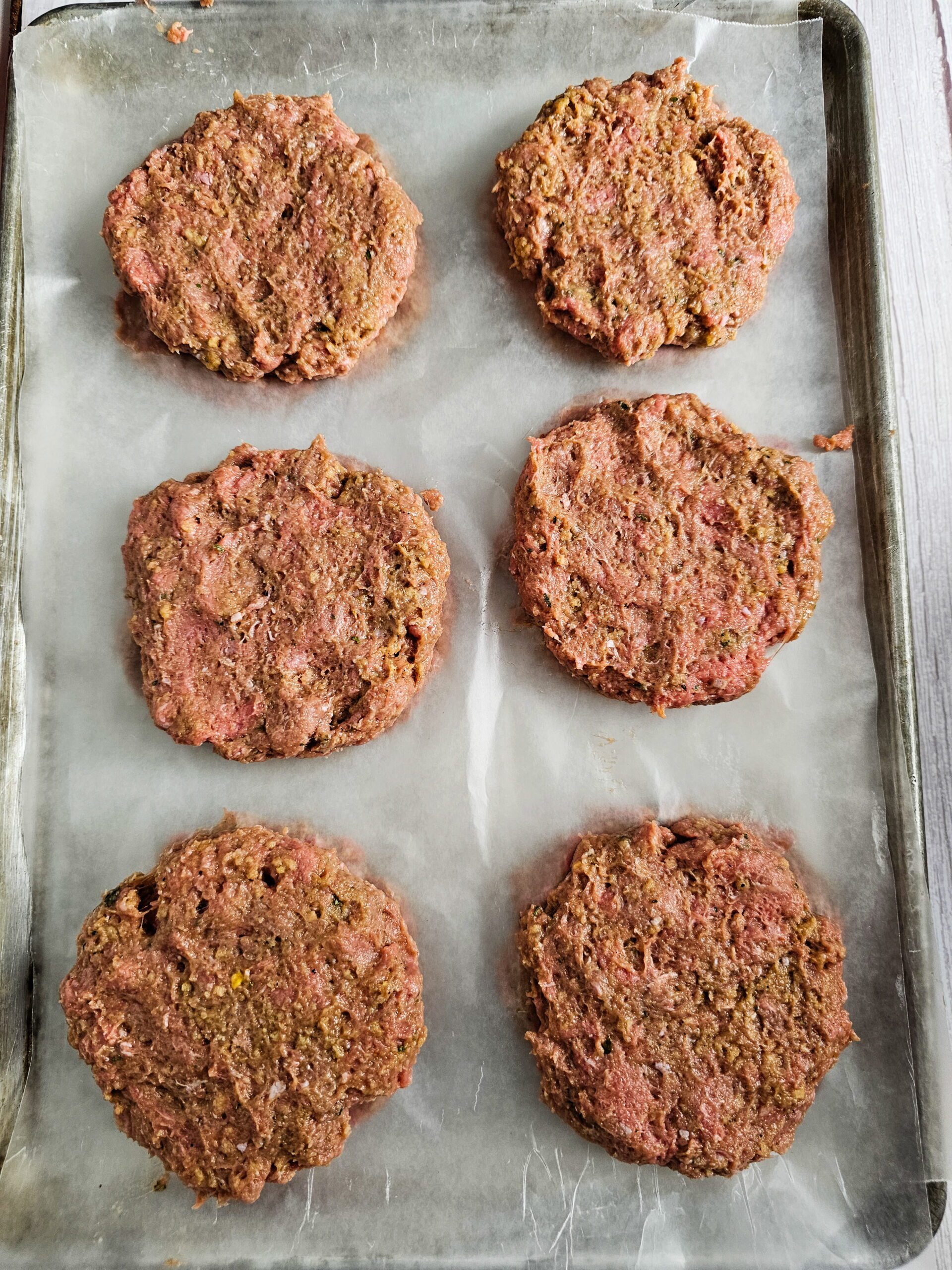 Raw turkey burger patties chilling on parchment paper in refrigerator before cooking