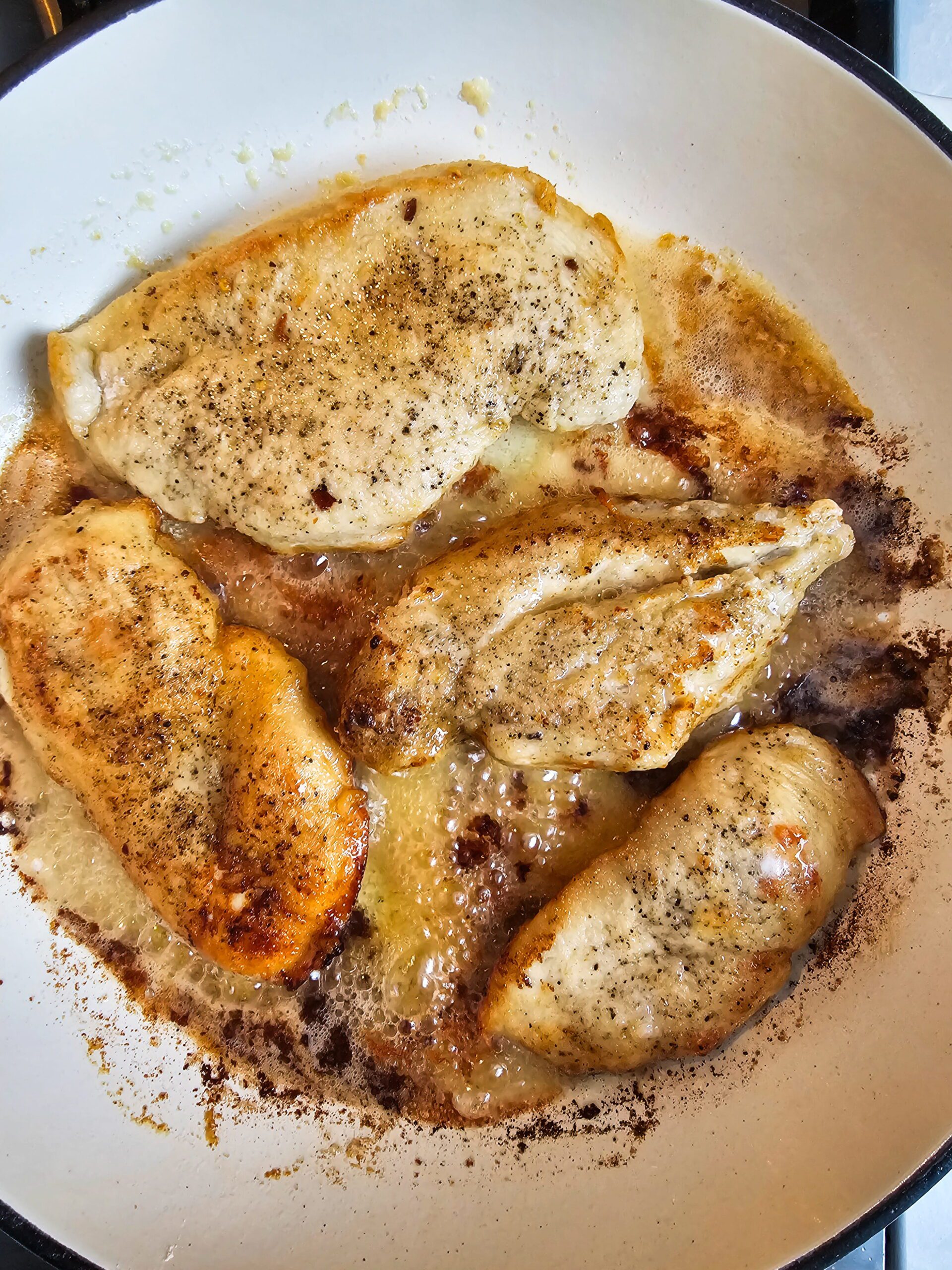 Flour-dredged chicken cutlets searing golden brown in butter and olive oil in a cast iron skillet