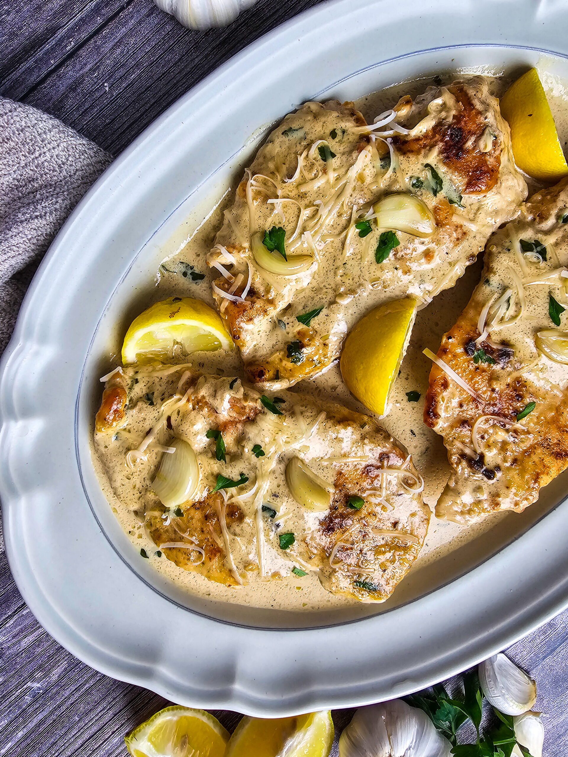 Restaurant style creamy garlic chicken served on an oval platter garnished with fresh parsley and lemon slices