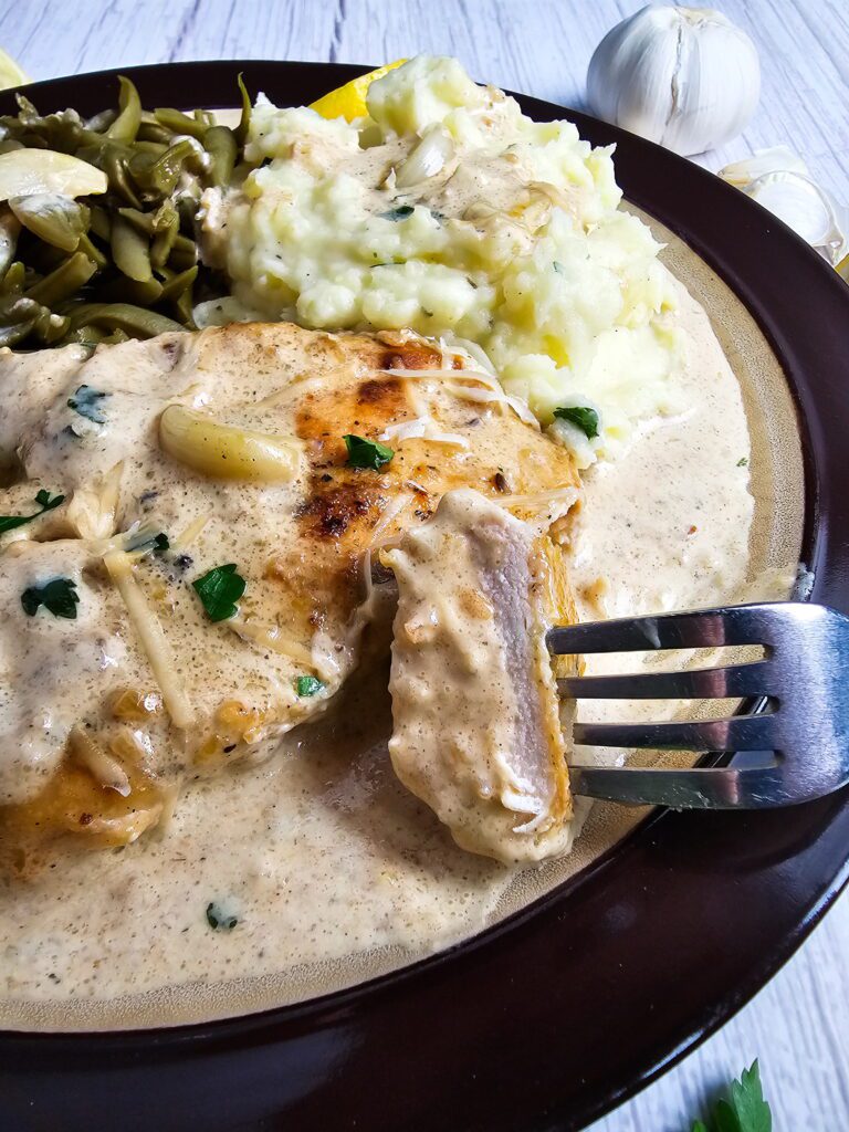 Overhead view of restaurant style creamy garlic chicken skillet with whole caramelized garlic cloves visible in the cream sauce