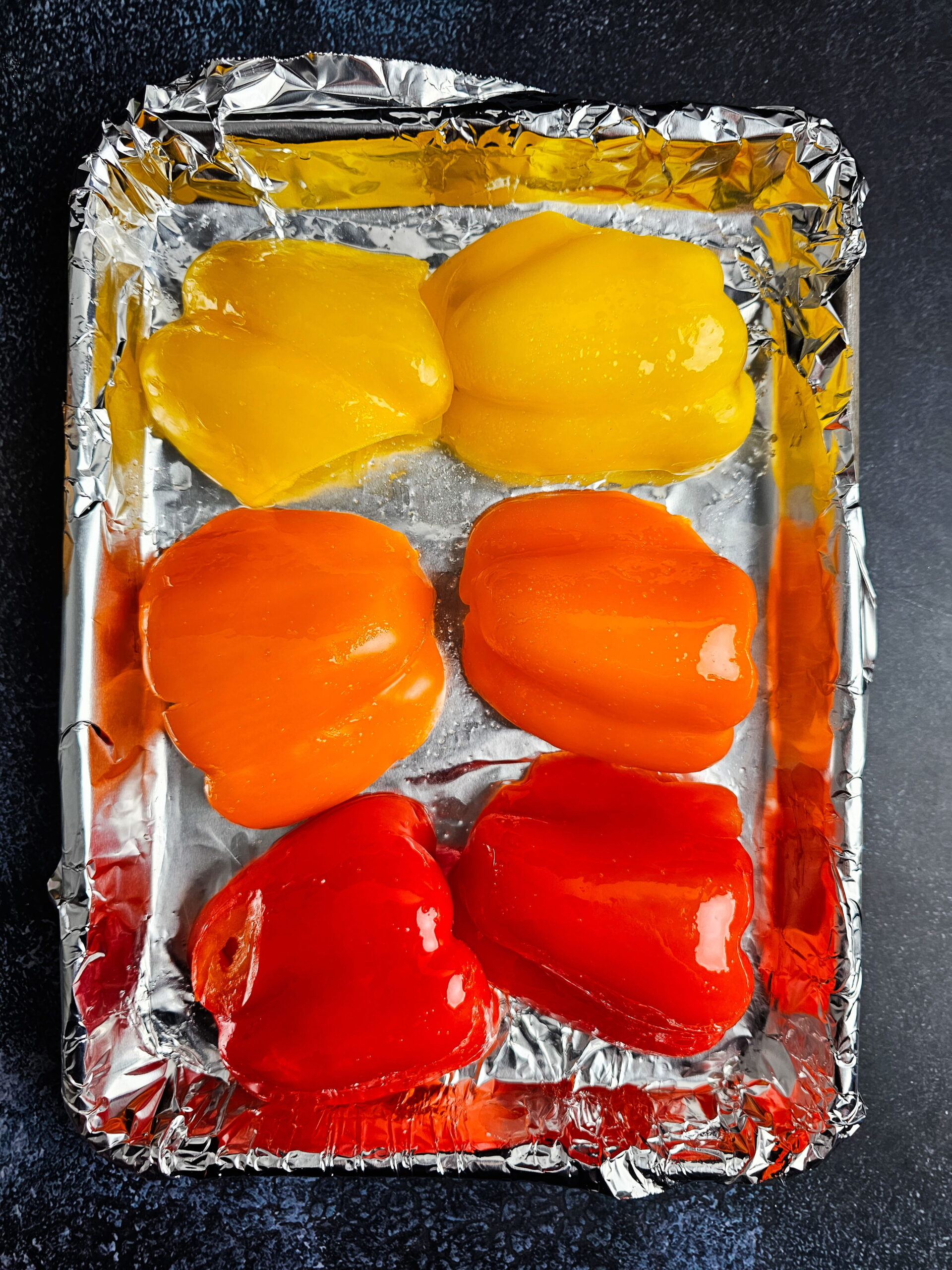 Whole red bell peppers blistered and charred on a sheet pan after roasting at 450 degrees