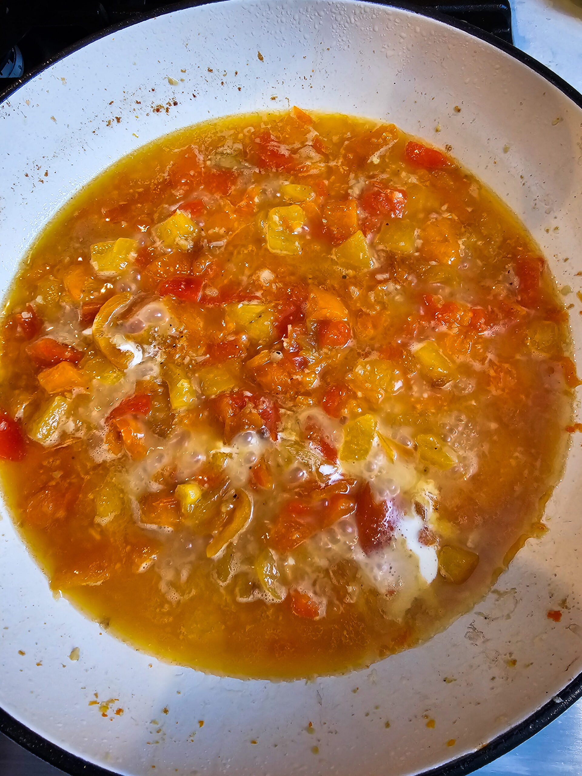 Roasted red pepper and chicken broth mixture simmering in skillet building the sauce base