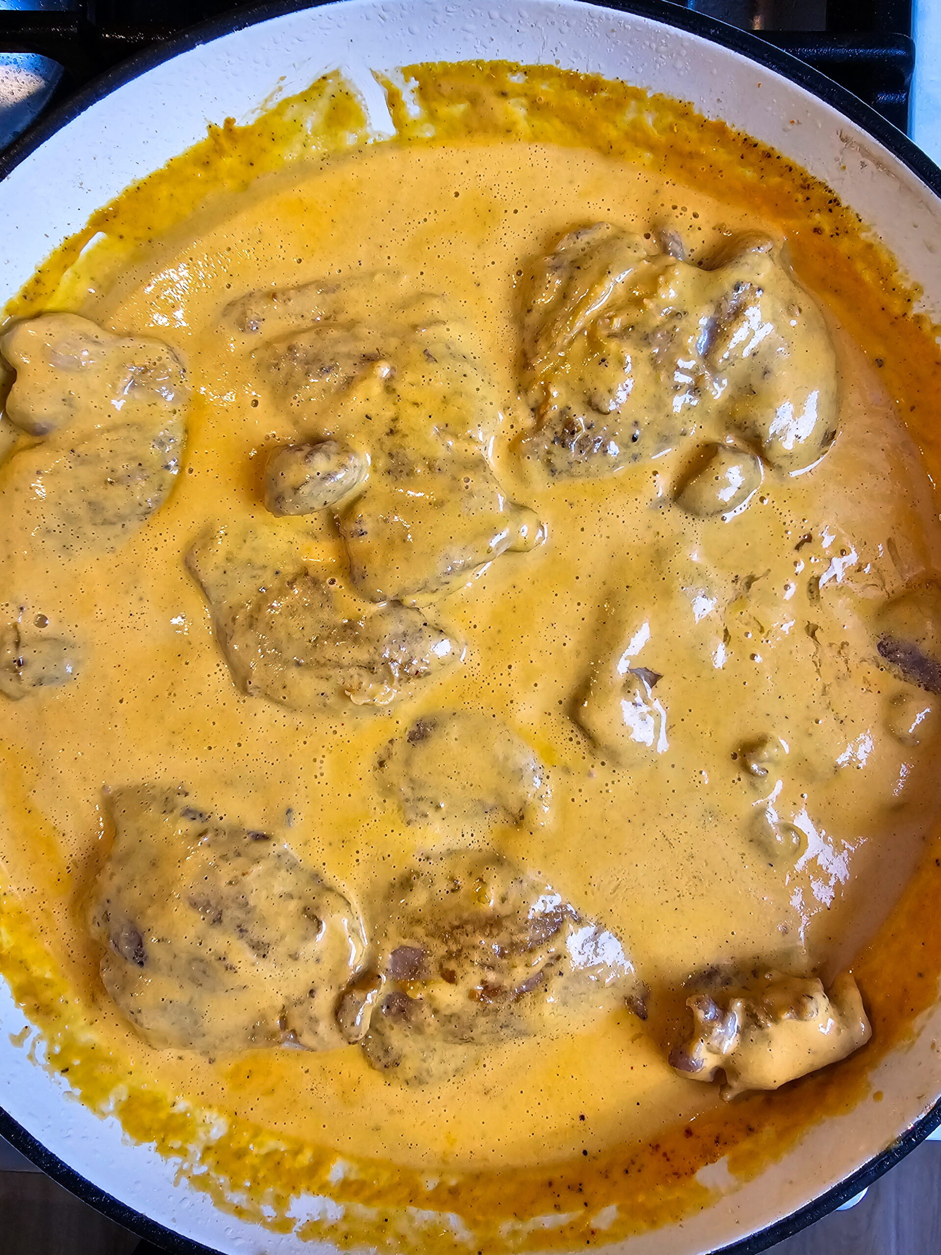 Seared chicken thighs returned to skillet coated in roasted red pepper cream sauce with crumbled goat cheese
