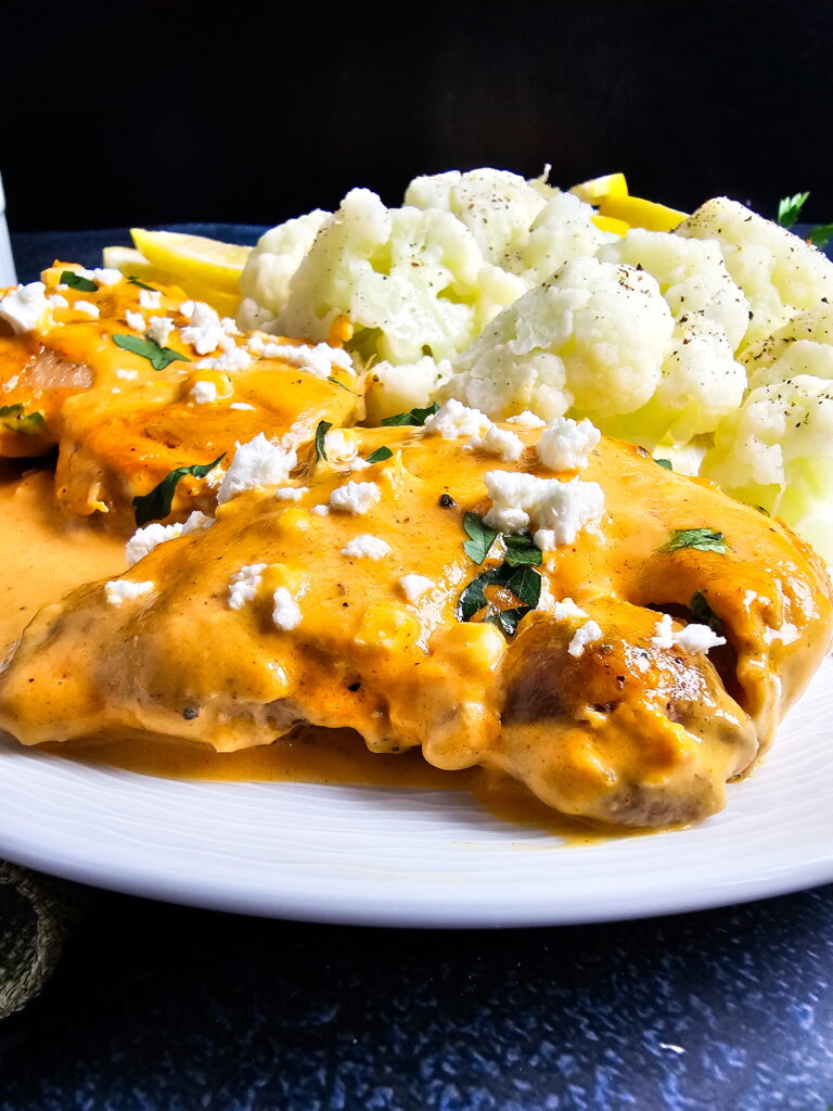 Chicken thighs in red pepper sauce served over cauliflower rice in a white bowl