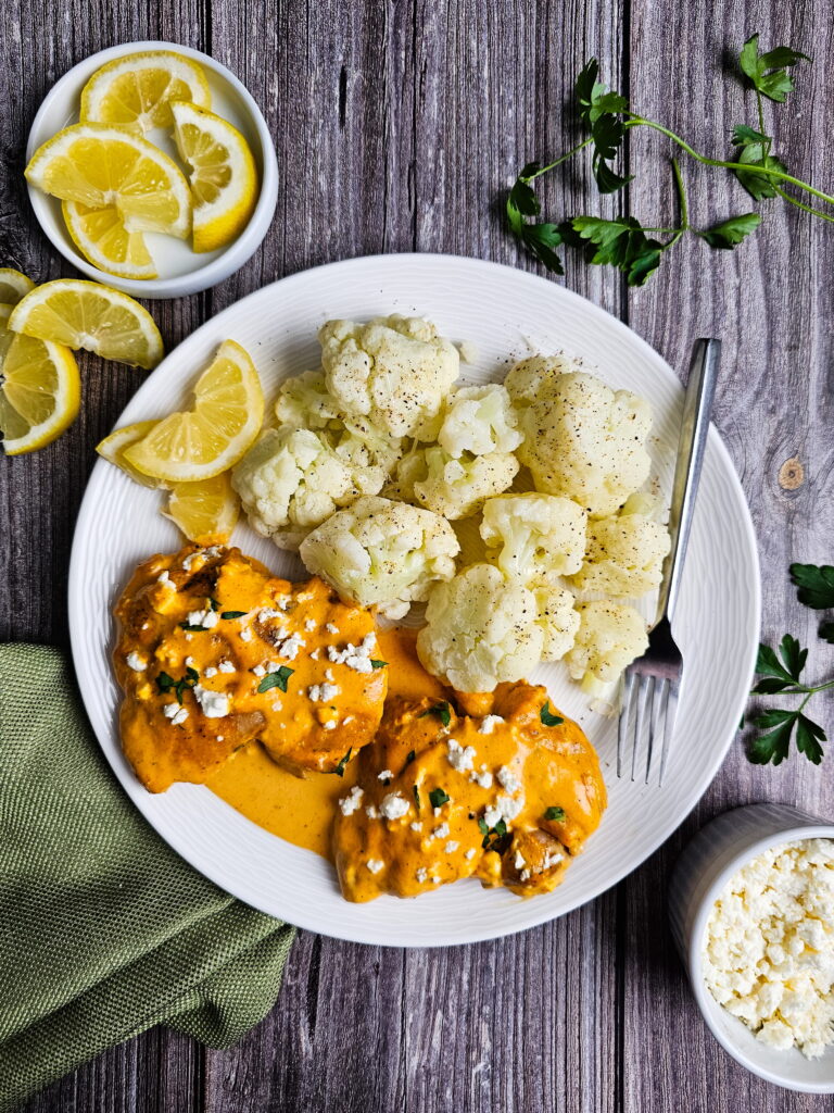 Close up of roasted red pepper cream sauce with chicken thighs and crumbled goat cheese