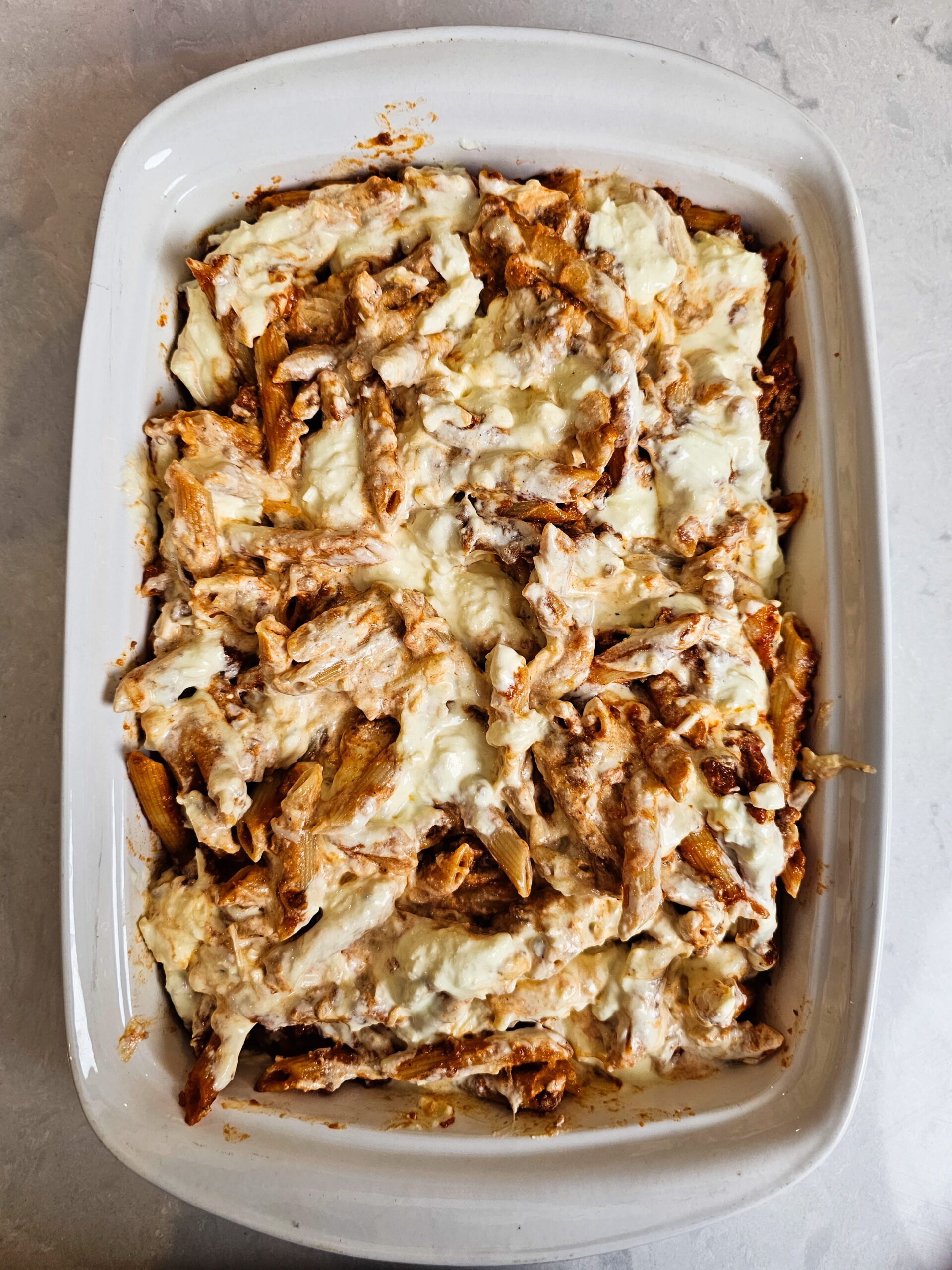 layering baked ziti with ricotta mixture and meat sauce in a 9x13 baking dish