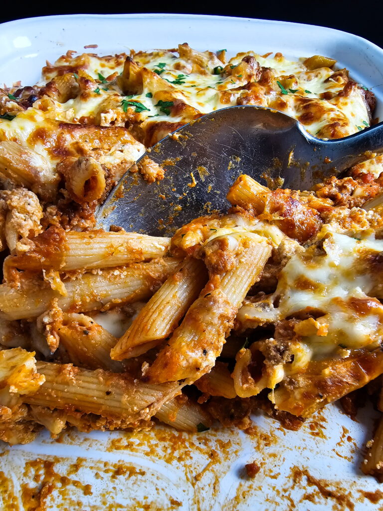 close-up of baked ziti with ricotta being served from a white casserole dish with a serving spoon