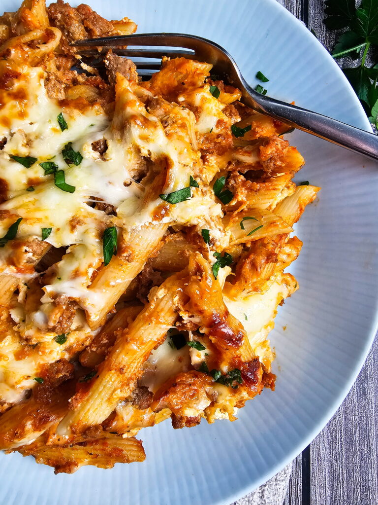 baked ziti with ricotta in a white baking dish with golden bubbly cheese and fresh basil on top