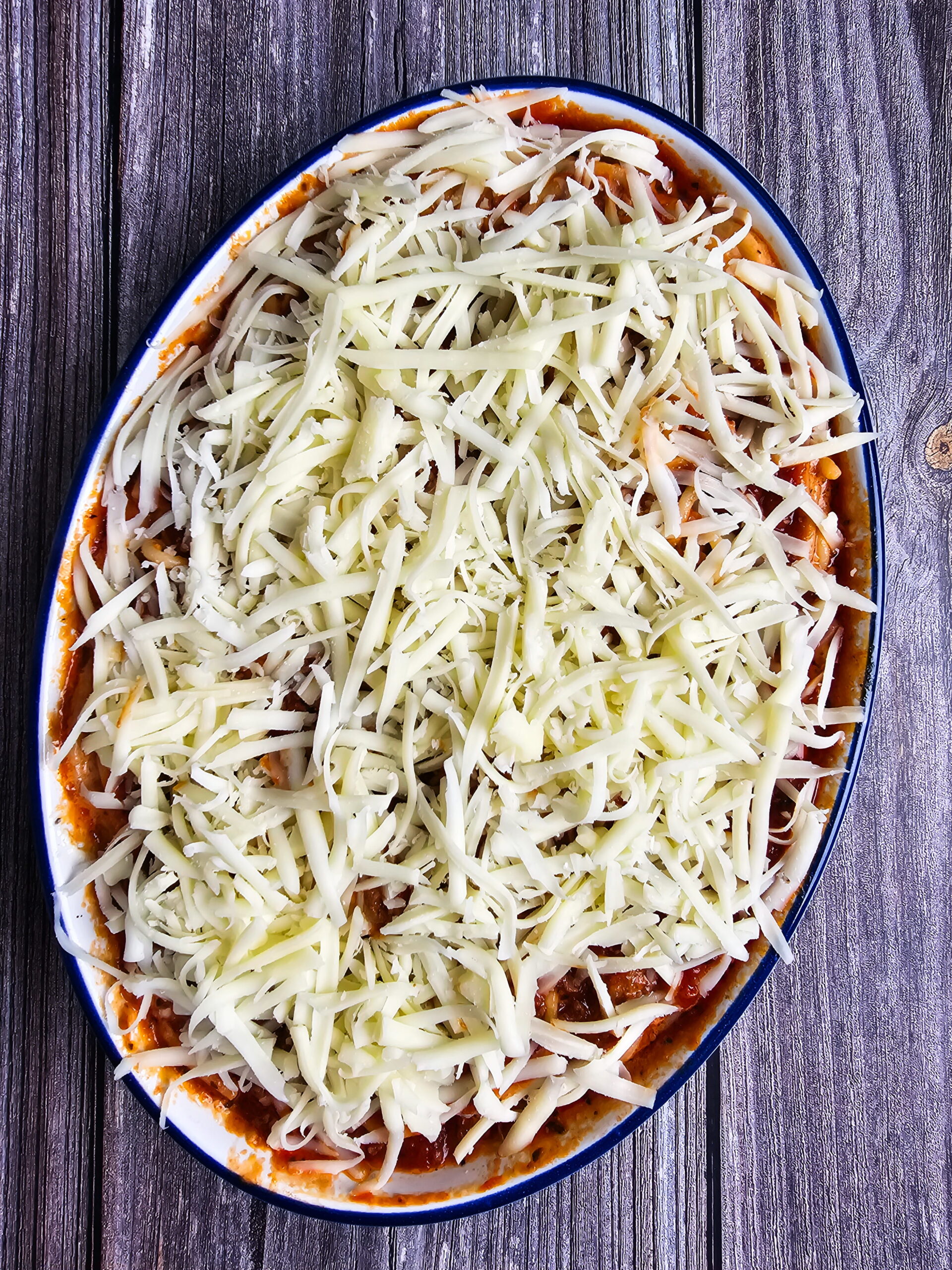 Assembled baked spaghetti casserole with Alfredo sauce topped with meat sauce and shredded mozzarella ready to bake