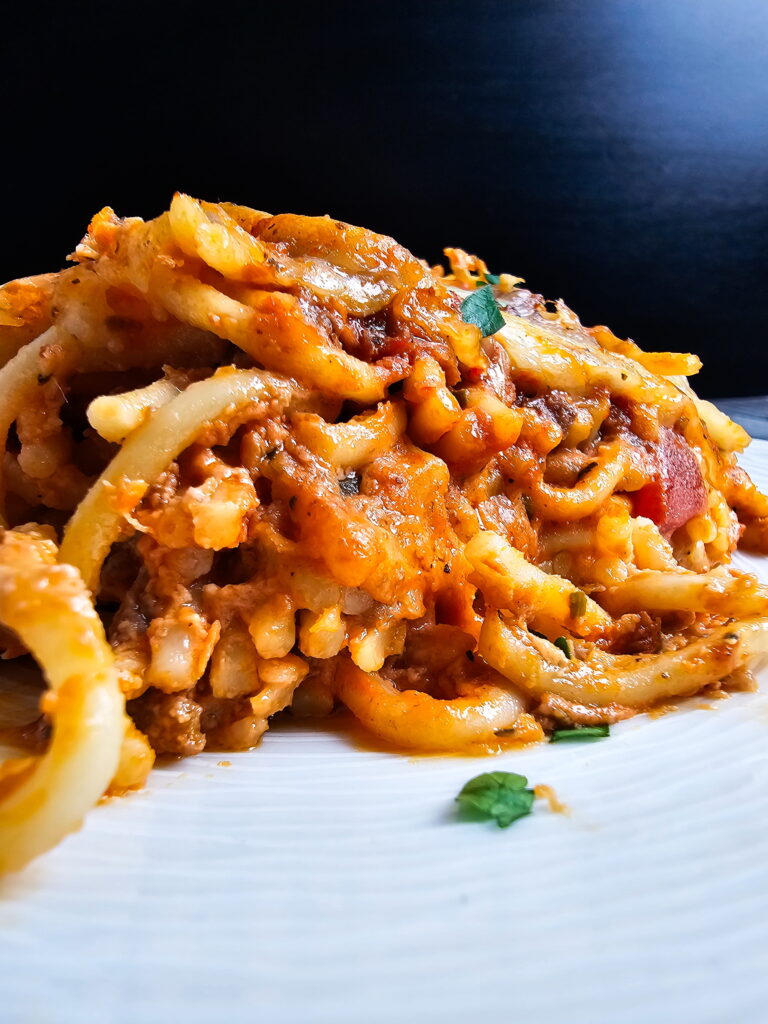 Single serving of baked spaghetti casserole with Alfredo sauce plated with a fork