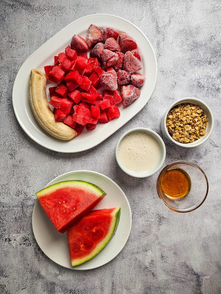 Overhead view of watermelon smoothie bowl topped with fresh blueberries strawberries coconut and granola on a light background