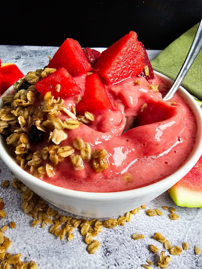 Watermelon strawberry smoothie bowl with granola fresh berries shredded coconut and mint leaves in a white bowl