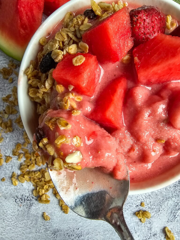 Close up of thick watermelon smoothie bowl with colorful toppings showing the spoonable texture and fresh fruit garnish