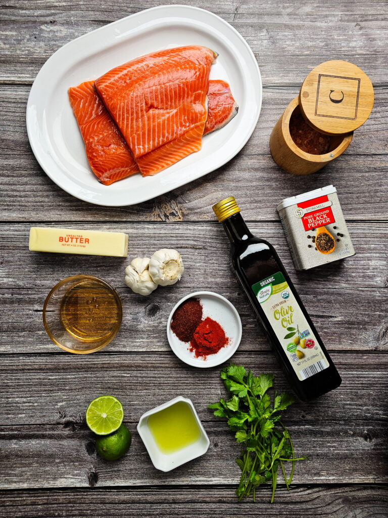 Ingredients for chili lime baked trout laid out including trout fillets, fresh lime, honey, smoked paprika, chili powder, garlic, and butter