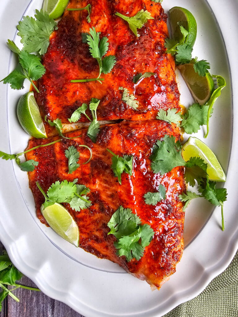 Overhead view of chili lime baked steelhead trout fillets on a parchment-lined baking sheet with cilantro and lime
